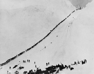 Miners climb, in single file, up the forbidding 45° trail of Chilkoot Pass.