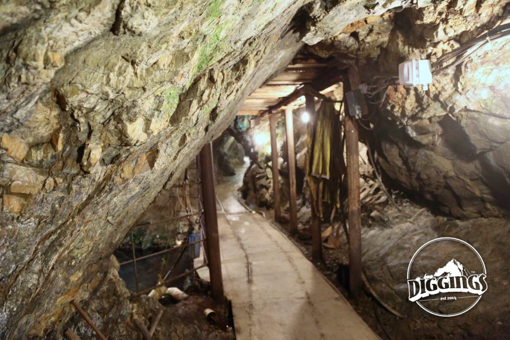 Walking through the  Crystal Gold Mine.  The original track for ore carts is still visible, embedded in the paved walkway.  To the right is an assortment of tools. the left is a flooded shaft that followed a vein deeper into the mountain.  To the right